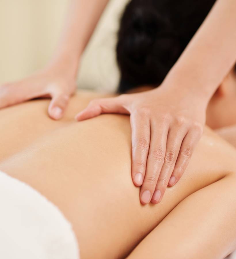 Hands of masseuse stroking back of female client to warm up the muscles